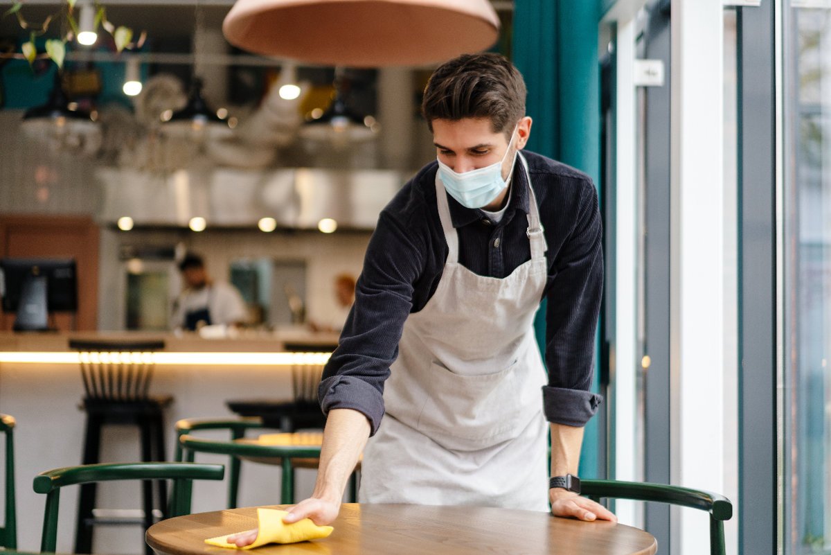 Waiter wearing mask and wiping down table