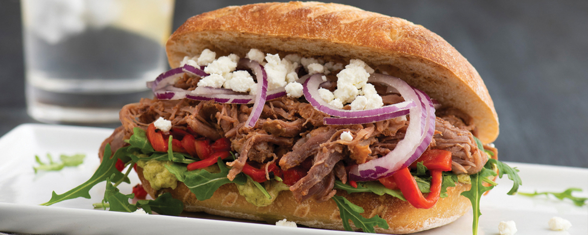 Pulled beef sandwich with onions goat cheese and toppings on a white plate