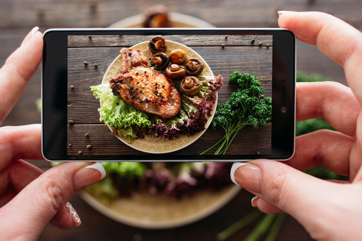 Lady holding iphone taking picture of chicken and mushrooms