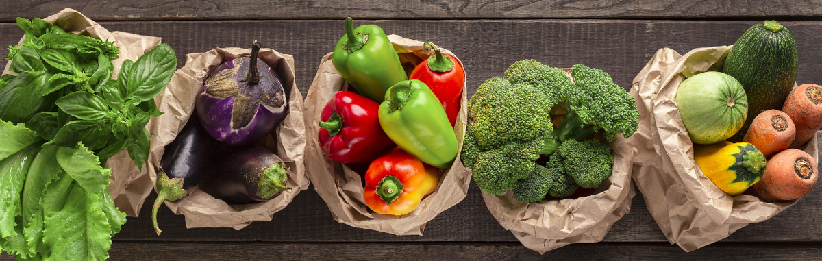 Bags of produce in brown paper bags on a wood background