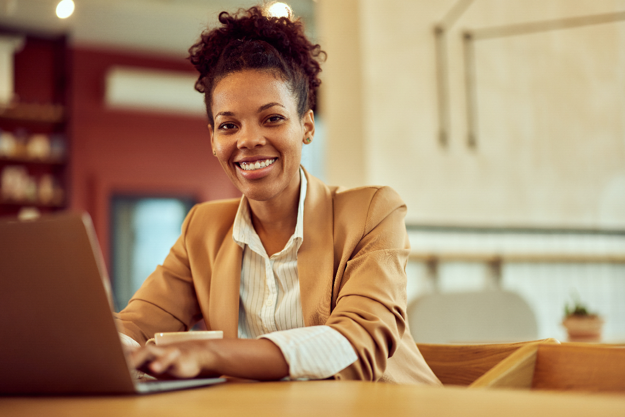 A female restaurant manager, working over the laptop, smiling for the camera.