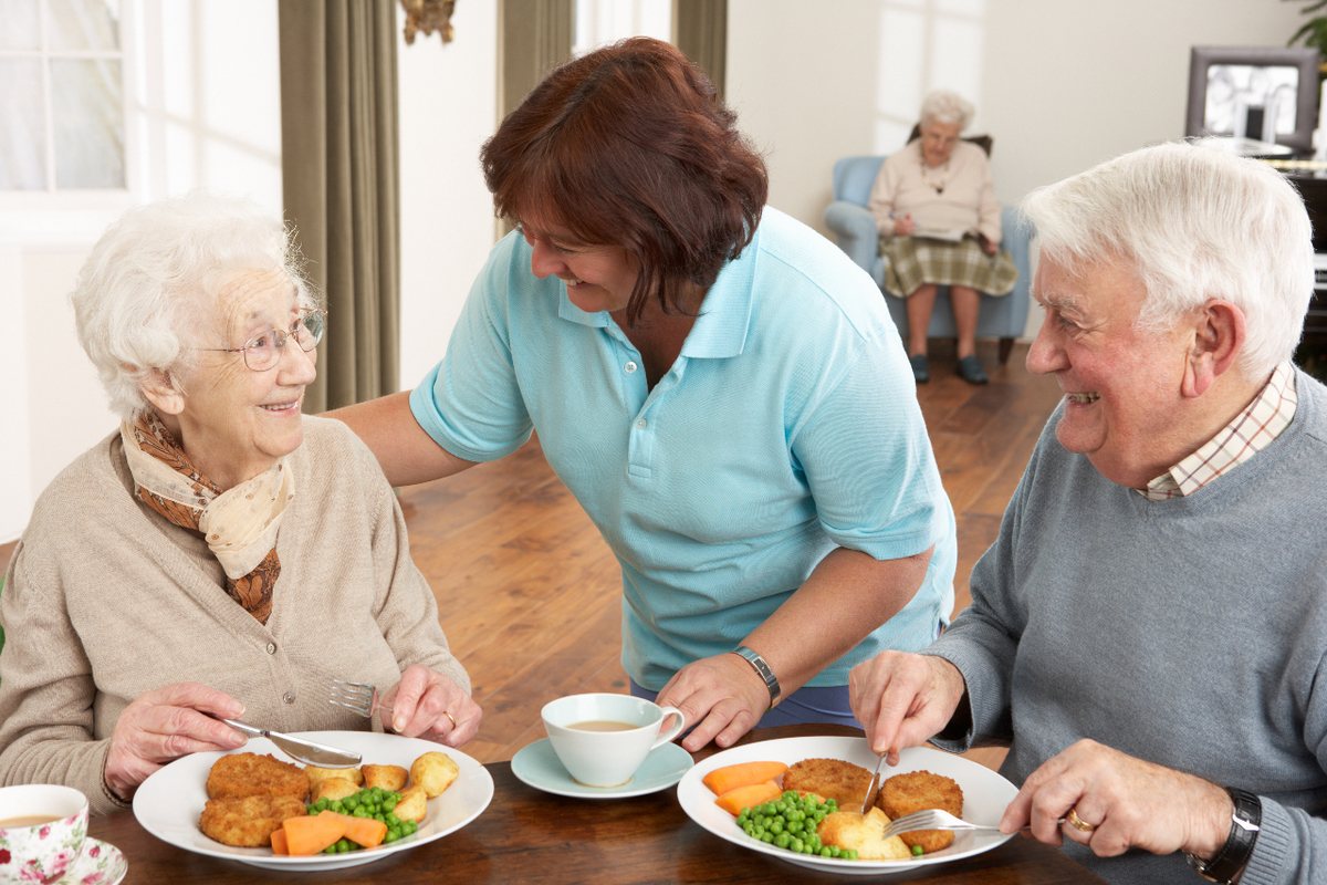 A healthcare worker speaking to an elderly couple enjoying a meal